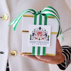 a person holding a christmas gift wrapped in green and white paper with a monogrammed ribbon