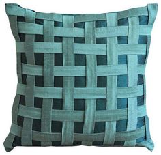 a blue pillow with woven squares on the front and back, sitting on top of a wooden table