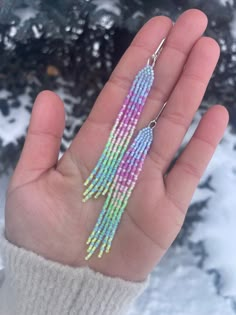 a hand holding a pair of colorful beaded tassels in front of snow covered ground