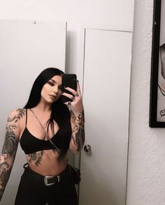 a woman with tattoos taking a selfie in front of a mirror and holding a cell phone