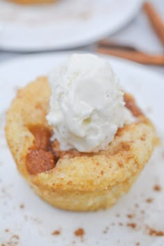 a small pastry with whipped cream on top sits on a plate next to cinnamon sticks