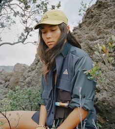 a woman sitting on the ground wearing a hat and holding her hands in her pockets