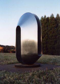 a large metal object sitting on top of a lush green field with trees in the background