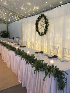 a long table with white linens and greenery is set up for a formal function