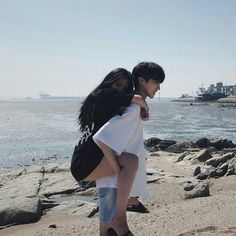 two people are standing on the beach with their backs to each other and looking at the water