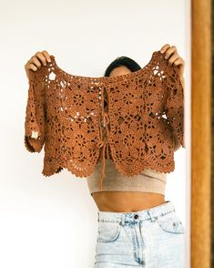 a woman holding up a crocheted sweater in front of her face