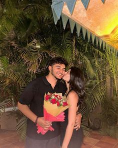 a man and woman kissing each other in front of some palm trees with flowers on them