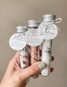 a hand holding four small bottles filled with different types of salts and spices, each containing an individual's name