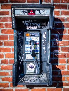 an old fashioned pay phone on the side of a brick building with graffiti all over it