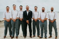 a group of men standing next to each other on top of a sandy beach in front of the ocean