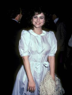 a woman in a blue and white dress holding a handbag smiling at the camera