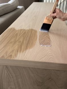 a person with a paintbrush on top of a wooden table next to a couch