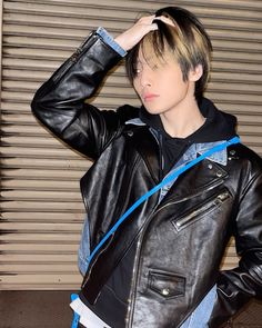 a young man wearing a black leather jacket and blue tape around his neck, standing in front of a garage door