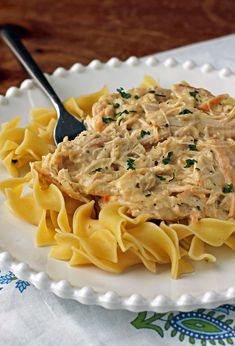 a white plate topped with pasta covered in chicken and sauce on top of it next to a fork