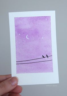 a person holding up a card with two birds sitting on a wire at the moon