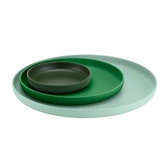 a green plate with a black bowl on the top and a white background behind it