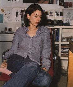 a woman sitting on top of a red chair in front of a desk and bookshelf