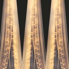 three white sheer curtains with lights on them