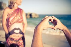 two people holding hands at the beach with one woman's stomach visible in front of her