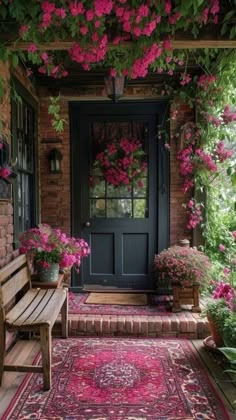 a porch with pink flowers on it and a bench in the foreground, next to a black door