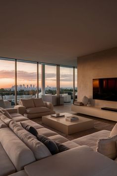 a living room with couches and a large window overlooking the cityscape at sunset