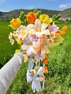 a person holding a bouquet of flowers in their hand on the side of a lush green field