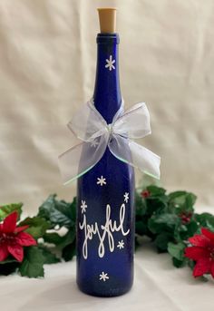 a blue glass bottle with a white ribbon on it and holly decorations around the neck