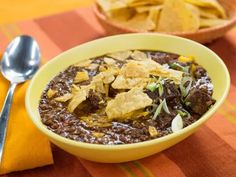 a bowl of chili and tortilla chips on a table with an orange napkin