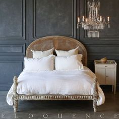 a bed with white linens and chandelier hanging from the wall behind it