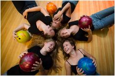 four girls are holding their bowling balls in the shape of a circle and smiling at the camera