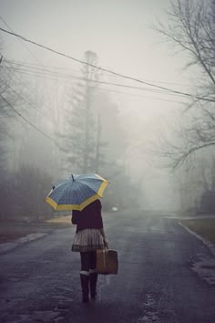 a woman holding an umbrella walking down the street in the rain with her purse and suitcase