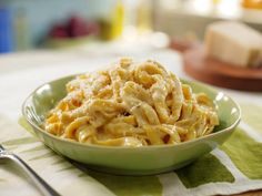 a green bowl filled with macaroni and cheese on top of a table next to a fork