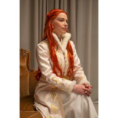 a woman with long red hair sitting on a couch wearing a white dress and fur collar