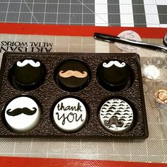 an assortment of buttons with mustaches and thank you written on them in a box