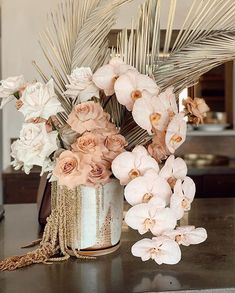 an arrangement of flowers in a tin can on a table with gold chains and palm leaves