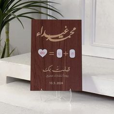 a wooden card with arabic writing and hearts in the middle, on a table next to a potted plant