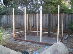 a wooden structure in the middle of a yard with rocks around it and trees behind it