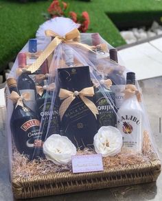 a basket filled with bottles of liquor and flowers on top of a stone table next to grass