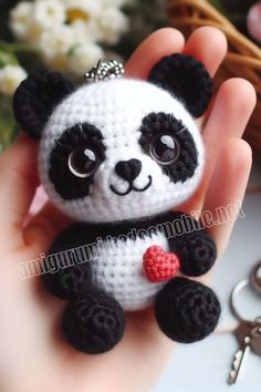 a hand holding a small crocheted panda bear with a heart on it's chest