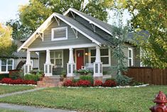 a gray house with red flowers in the front yard