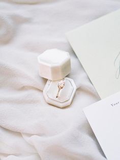 a ring with a diamond in it sitting on top of a white sheet next to a note