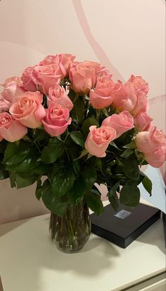 a vase filled with pink roses sitting on top of a white table next to a black box