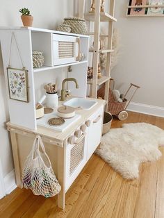 a white play kitchen with lots of shelves and baskets on the top shelf next to it