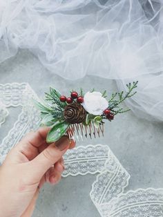 a person holding a comb with flowers and pineconis on it, in front of white lace