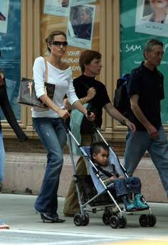 a woman pushing a baby in a stroller while walking down the street with other people