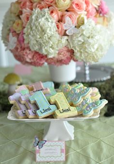 there is a cake and cookies on the table with flowers in the vase behind it