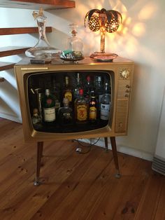 an old fashioned television with liquor bottles on it's side table next to a lamp