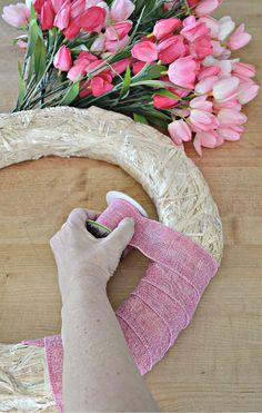 someone is making a wreath out of wicker and fabric with pink flowers in the background