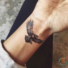 a black and white bird tattoo on the left wrist, with an eagle flying above it