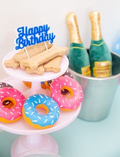 a birthday cake with doughnuts and dog treats on the table next to champagne bottles